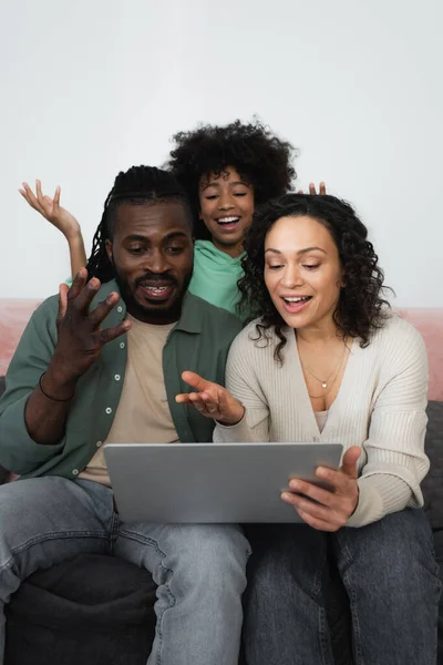 Familia afro-americana emocional gesto mientras ve la película en el ordenador portátil en la sala de estar - foto de stock