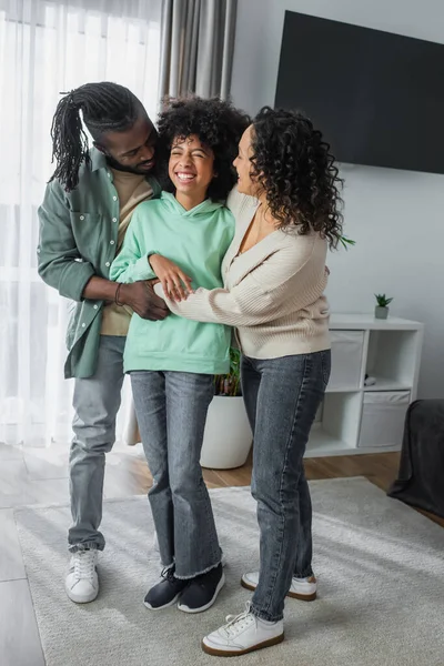 Pleine longueur de heureux parents afro-américains étreignant gaie fille préadolescente à la maison — Photo de stock