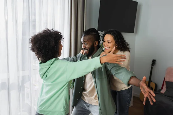 Feliz africana americana chica abrazando alegre padres en casa - foto de stock