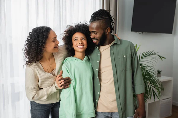 Felici genitori afro-americani che abbracciano la figlia allegra e riccia a casa — Foto stock