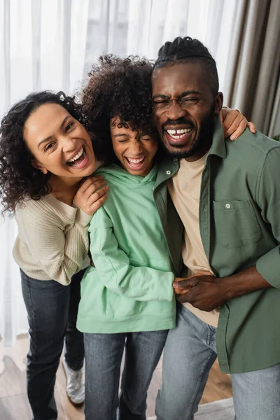 Familia afroamericana feliz abrazándose y riéndose en casa - foto de stock