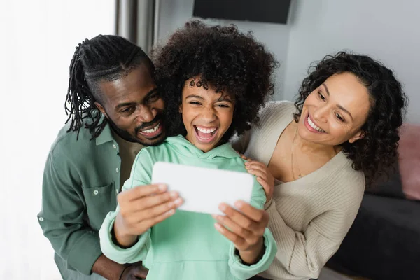 Happy preteen african american kid taking selfie with parents on smartphone at home — Stock Photo