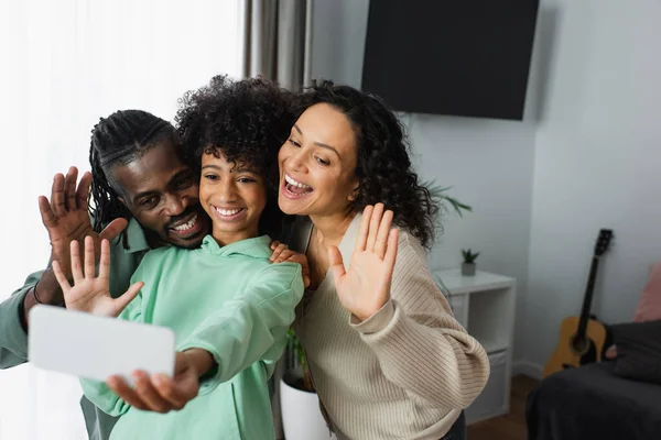 Allegra famiglia afro-americana che sorride e agita le mani durante la videochiamata sullo smartphone — Foto stock