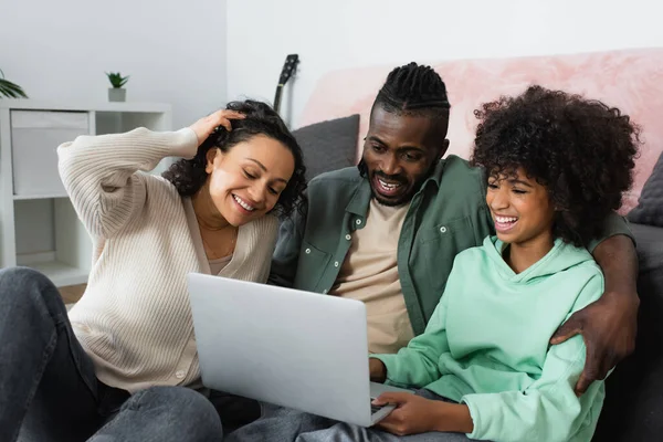 Alegre afroamericano familia sonriendo y viendo la película en el ordenador portátil en casa - foto de stock