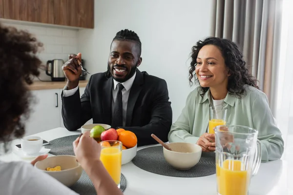 Fröhliche afrikanisch-amerikanische Eltern blicken ihre Tochter beim Frühstück an — Stockfoto