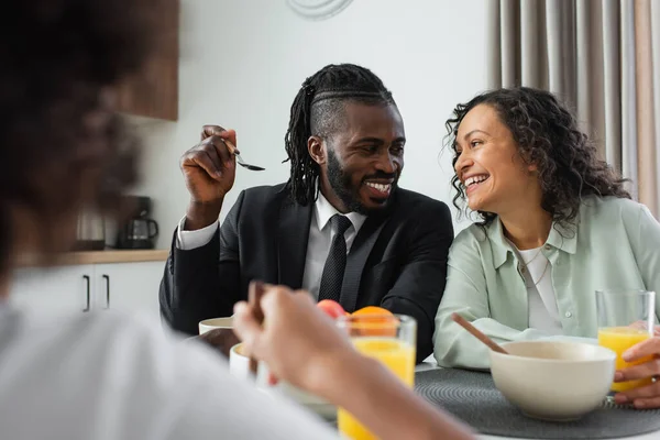 Happy african american parents looking at each other near blurred daughter during breakfast — Stock Photo