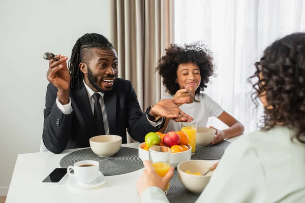 Homem americano africano feliz no terno que fala com a esposa perto da filha preteen durante o café da manhã — Fotografia de Stock