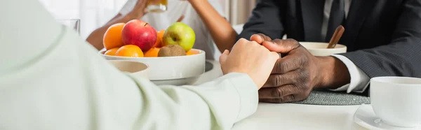 Cropped view of african american man in suit holding hands with wife near daughter during breakfast, banner — Stock Photo