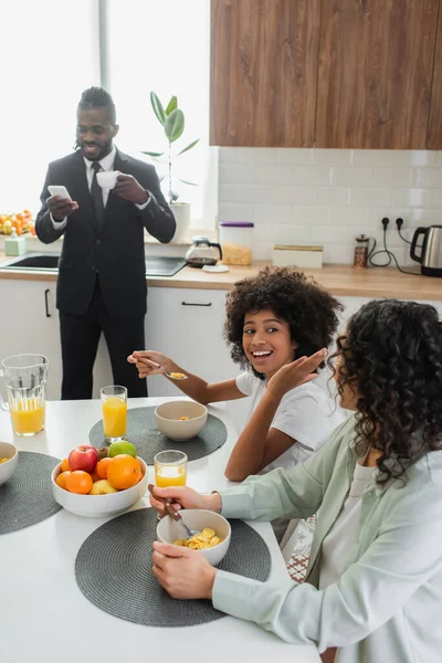 Glückliches afrikanisch-amerikanisches Mädchen schaut Mutter beim Frühstück in der Nähe des Vaters im Anzug an — Stockfoto