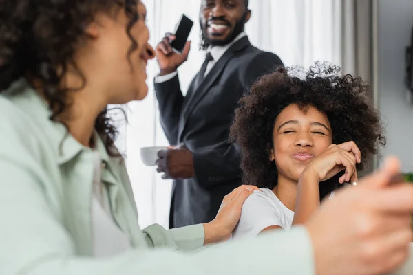 Feliz menina afro-americana soprando bochechas perto de mãe em primeiro plano borrado — Fotografia de Stock