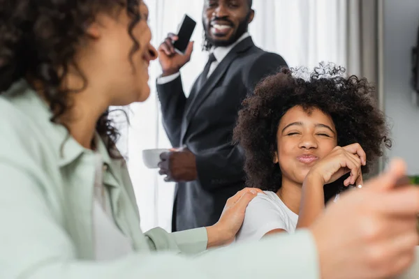 Feliz africana americana chica soplando mejillas cerca de madre en borrosa primer plano - foto de stock