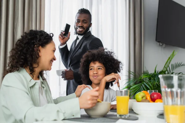 Happy african american girl puffing cheeks while eating breakfast near parents — Stock Photo
