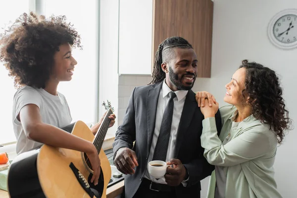 Happy african american preteen girl playing acoustic guitar near cheerful parents — Stock Photo