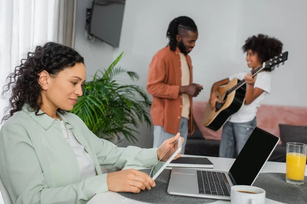 Curly african american woman holding digital tablet near laptop and drinks on desk — Stock Photo