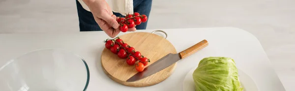 Vista parcial del hombre sosteniendo tomates cherry maduros cerca de lechuga fresca y tabla de cortar con cuchillo, pancarta - foto de stock