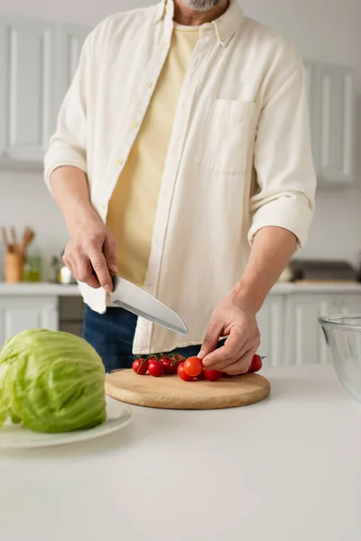 Частичный вид человека в белой рубашке с ножом рядом с помидорами черри на доске — стоковое фото