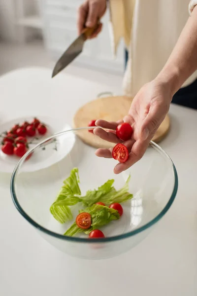 Partial view of man holding halves of cherry tomato while preparing fresh salad in kitchen — Stock Photo