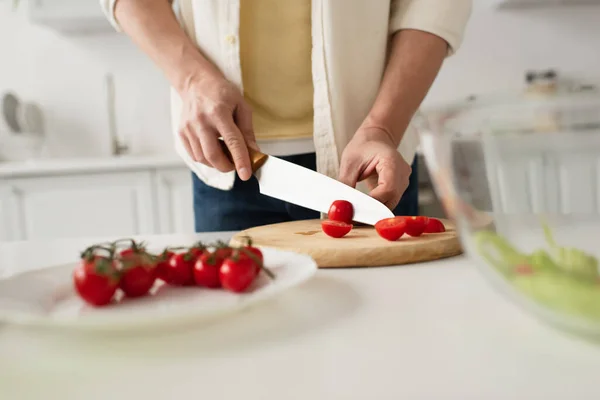 Vue partielle de l'homme coupant des tomates cerises sur planche à découper au premier plan flou — Photo de stock