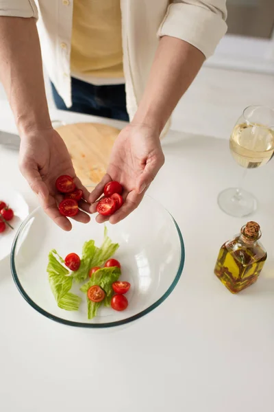 Vue du dessus de l'homme cultivé tenant des tomates cerises coupées près d'un bol avec salade et bouteille d'huile — Photo de stock