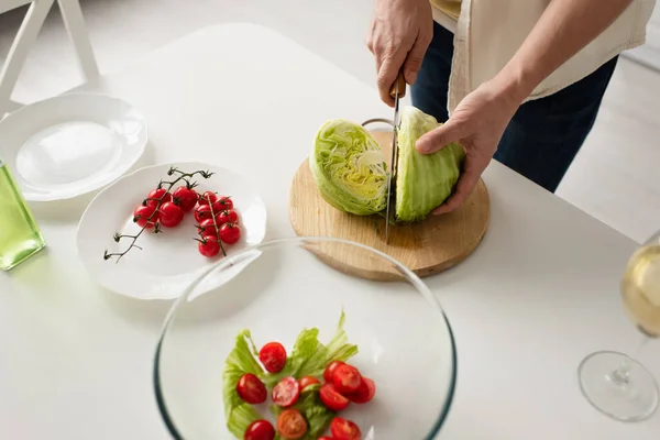 Vista superior do homem cortado cortando alface fresca perto de tomates cereja maduros e tigela com salada — Fotografia de Stock