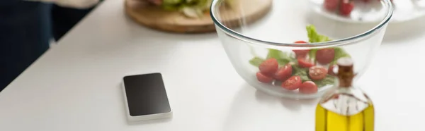 Telefono cellulare con schermo bianco vicino alla ciotola con insalata di verdure e bottiglia di olio, banner — Foto stock