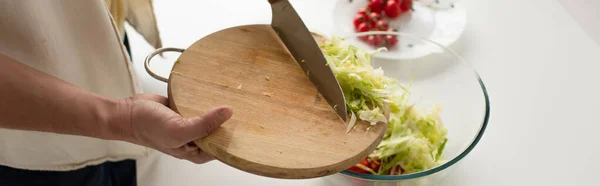 Vue partielle de l'homme avec planche à découper ajoutant de la laitue coupée dans un bol lors de la préparation de salade de légumes, bannière — Photo de stock