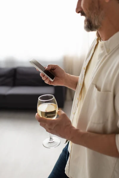 Cropped view of blurred man with glass of white wine using smartphone with blank screen — Stock Photo