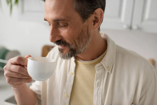 Bearded man in white shirt enjoying flavor of morning coffee at home — Stock Photo