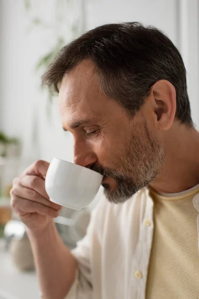 Retrato de hombre con barba gris disfrutando de café de la mañana sobre fondo borroso - foto de stock
