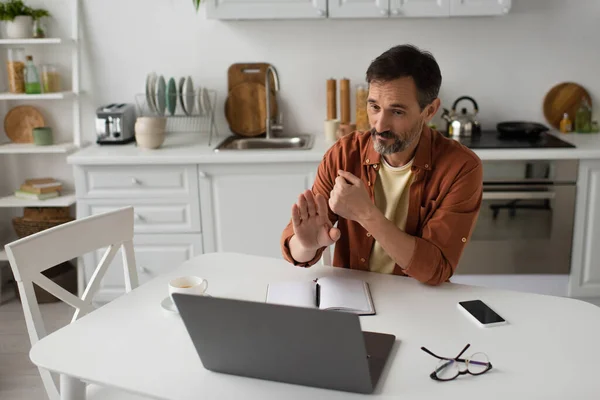 Homem barbudo gesto durante conferência on-line no laptop perto de notebook vazio e celular com tela em branco — Fotografia de Stock