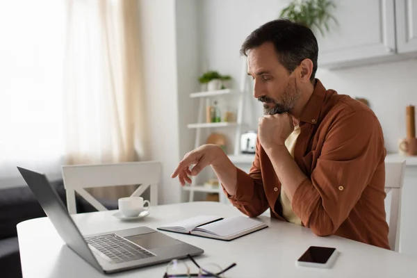 Pensive man thinking near empty notebook and gadgets in kitchen — Stock Photo