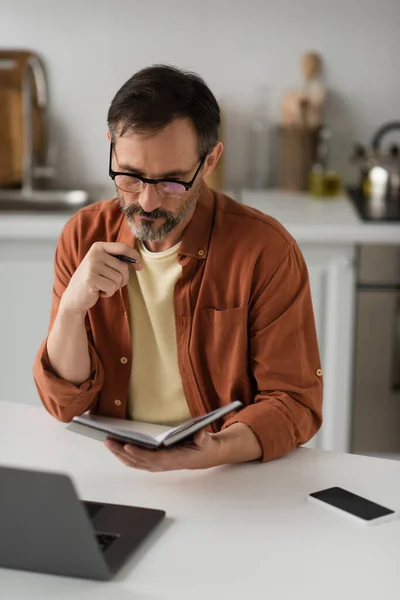 Cher homme dans les lunettes de vue regardant portable près flou ordinateur portable et téléphone mobile avec écran blanc — Photo de stock