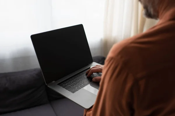 Partial view of blurred man using laptop with blank screen at home — Stock Photo