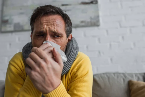 Homem doente em cachecol quente que sofre de rinite e segurando guardanapo de papel perto do rosto — Fotografia de Stock