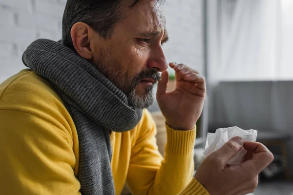 Sick man with sore throat and runny nose wearing warm scarf and holding paper napkin — Stock Photo