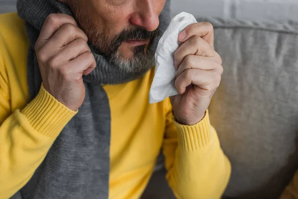 Partial view of ill man in warm scarf holding paper napkin — Stock Photo