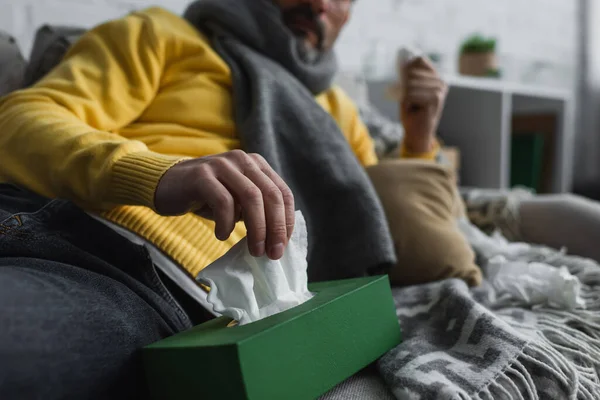 Teilbild eines kranken Mannes, der auf Couch liegt und Papierserviette aus Packung nimmt — Stockfoto