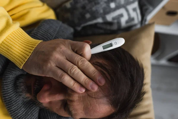 Vue de dessus de l'homme malade tenant le thermomètre et souffrant de maux de tête — Photo de stock