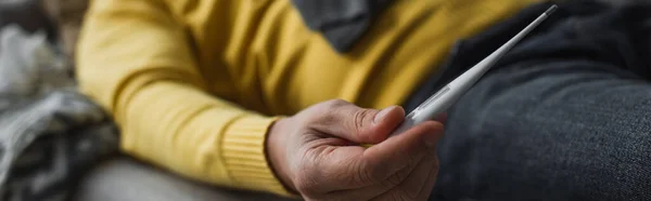 Partial view of diseased man holding electronic thermometer while lying on blurred background, banner — Stock Photo