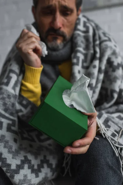 Foco selectivo de paquete con servilletas de papel en la mano del hombre enfermo sobre fondo borroso - foto de stock