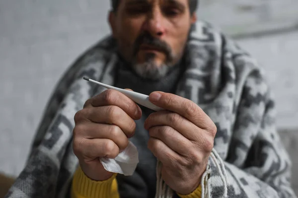 Selective focus of electronic thermometer in hands of ill man on blurred background — Stock Photo