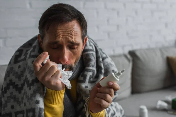 Ill man with closed eyes suffering from runny nose and holding nasal spray with paper napkin — Stock Photo