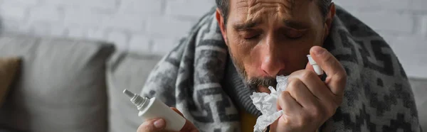 Diseased man with closed eyes holding paper napkin and nasal spray, banner — Stock Photo