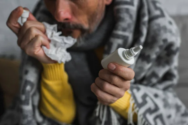 Partial view of blurred man holding nasal spray and crumpled paper napkin while suffering from runny nose — Stock Photo