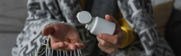 Partial view of ill man under warm blanket holding container and pill, banner — Stock Photo