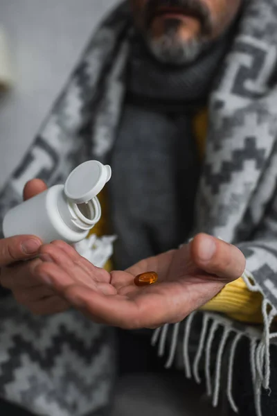 Cropped view of diseased man holding container and pill on blurred background — Stock Photo