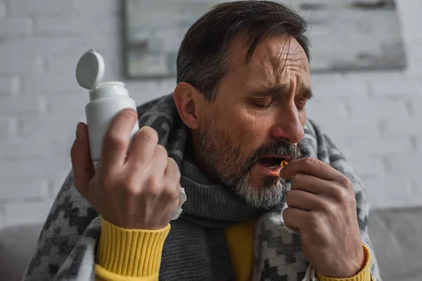 Hombre enfermo con los ojos cerrados sosteniendo el envase y tomando la píldora en casa - foto de stock