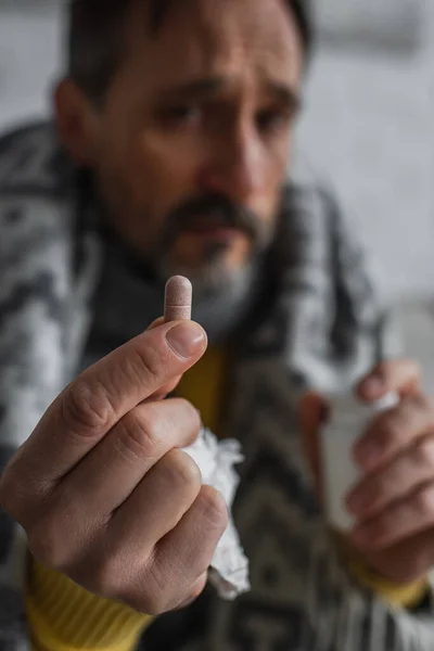 Enfoque selectivo de la píldora en la mano del hombre enfermo sobre fondo borroso - foto de stock