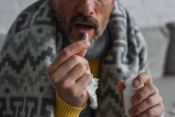 Partial view of diseased man with paper napkin taking pill on blurred background — Stock Photo