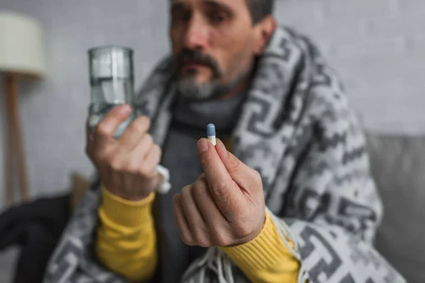 Hombre enfermo sosteniendo píldora y vaso de agua sobre fondo borroso - foto de stock
